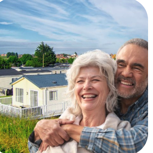 A happy retired couple at a UK holiday park, with caravans and a fence in the background.